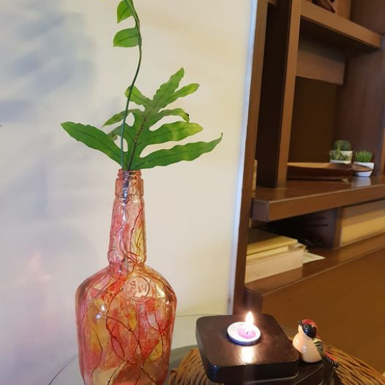 Upcycled liquor bottle simply painted to becone a planter or a vase. Upcycled packaging wood candle holder accessorized with an etikoppaka handpainted bird. Both sitting on a table mat upcycled from newspaper.
